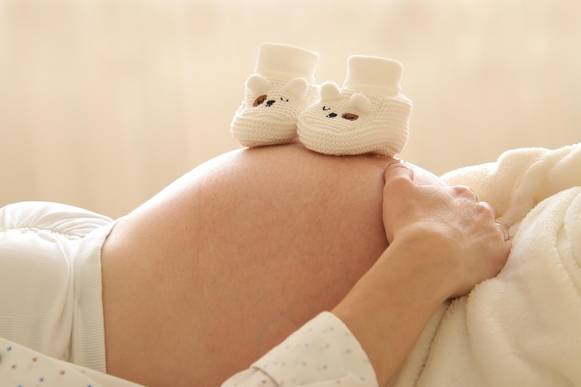The image shows a pregnant woman's baby bump with baby shoes placed on top of it.