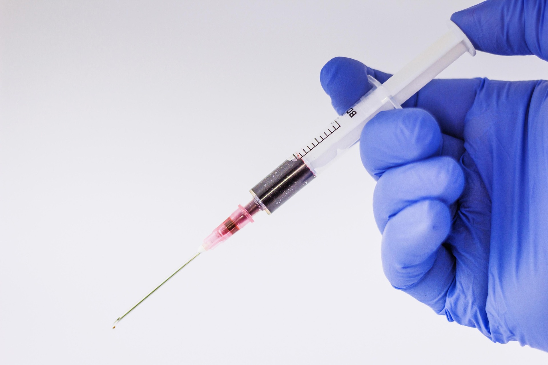 The image shows a medical practitioner's gloved hand holding a syringe. It represents a Beta hCG blood test after frozen embryo transfer.